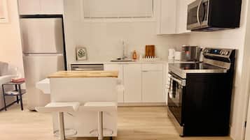 Una cocina compacta con refrigerador, microondas, estufa y un pequeño comedor con taburetes.