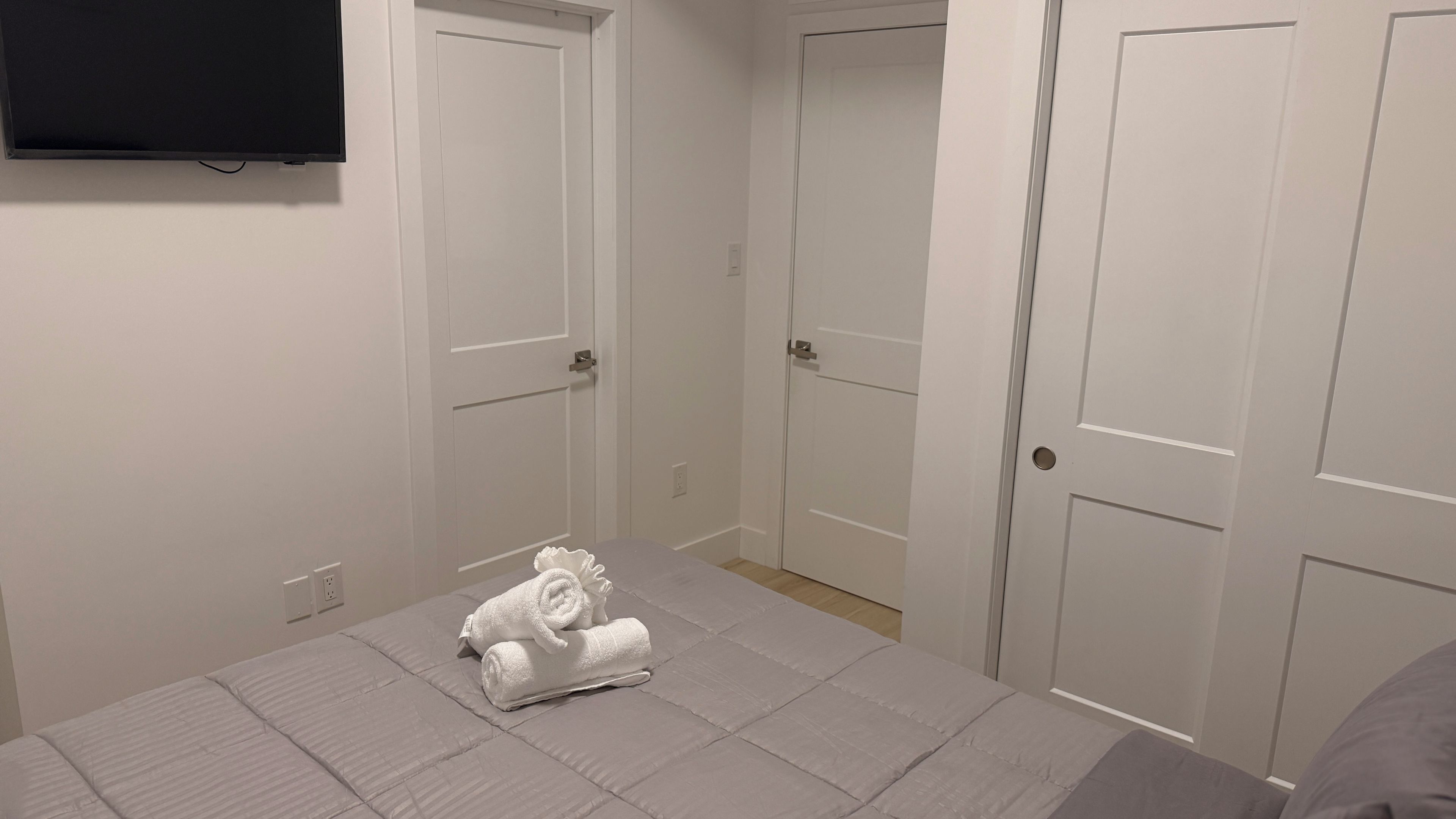 A bedroom with a bed, a flat-screen TV mounted on the wall, and a set of white doors.