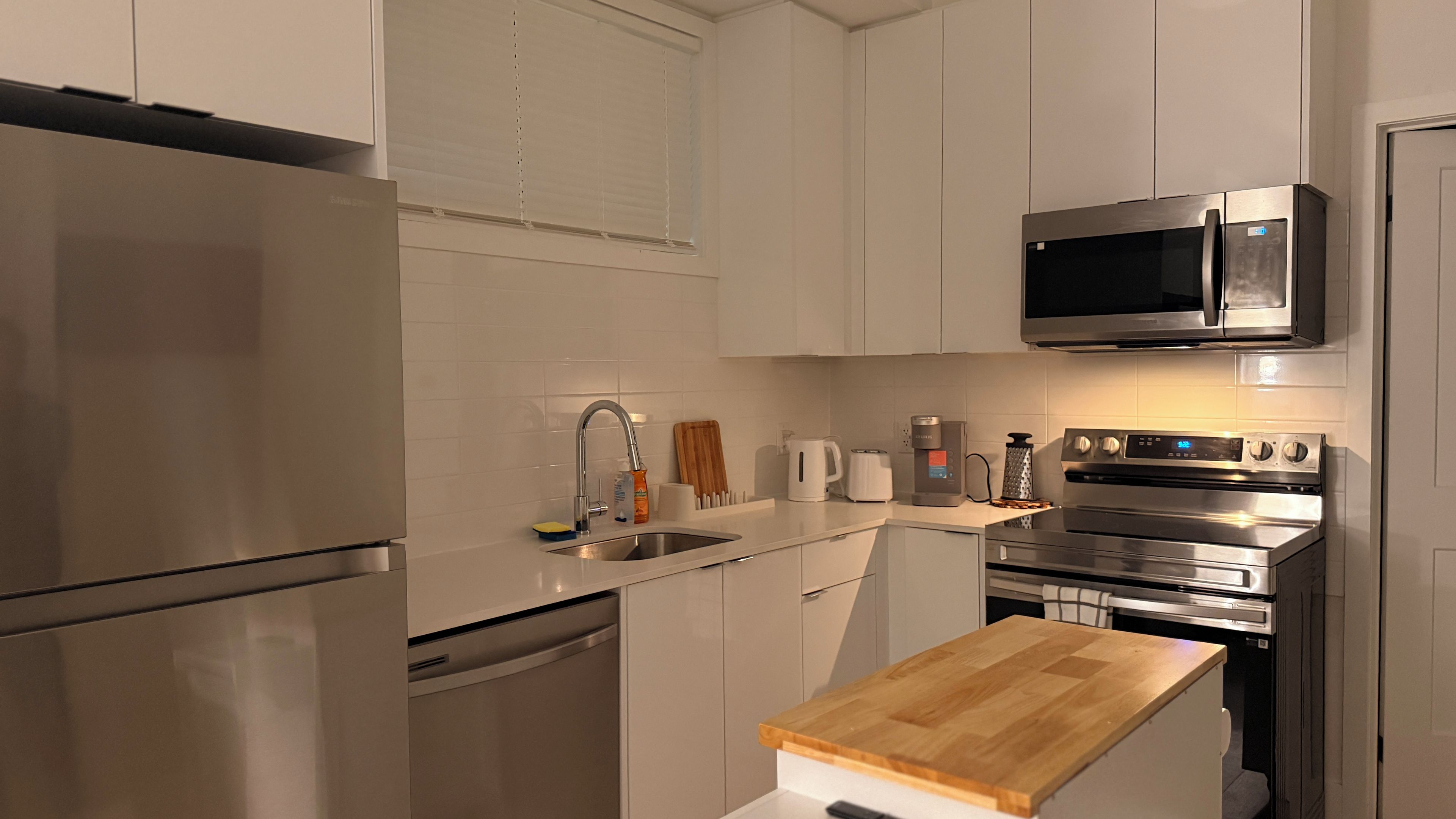A modern kitchen with stainless steel appliances, a wooden countertop, and white cabinetry.