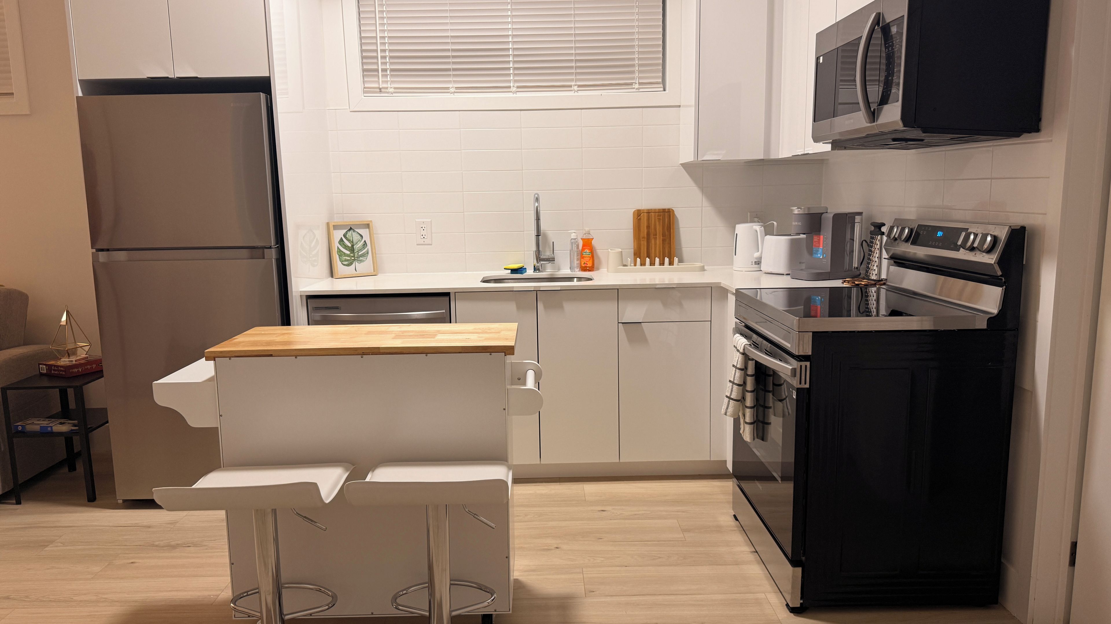 Una cucina moderna con forno a incasso, microonde e un piccolo angolo ristoro con tavolo e sedie bianche.