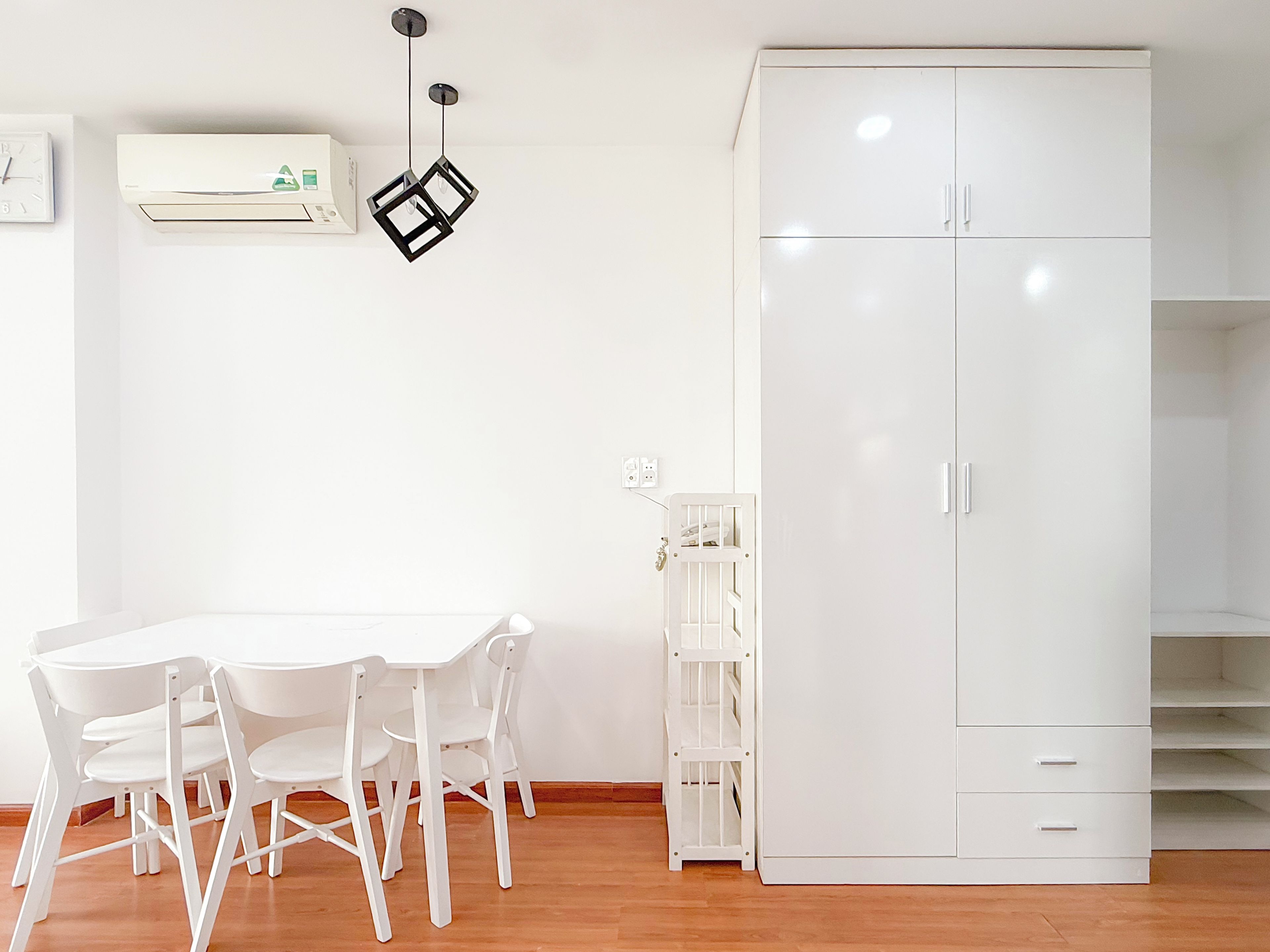 Una habitación con una mesa y sillas blancas, un armario blanco y una lámpara colgante.