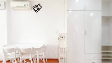 Una habitación con una mesa y sillas blancas, un armario blanco y una lámpara colgante.