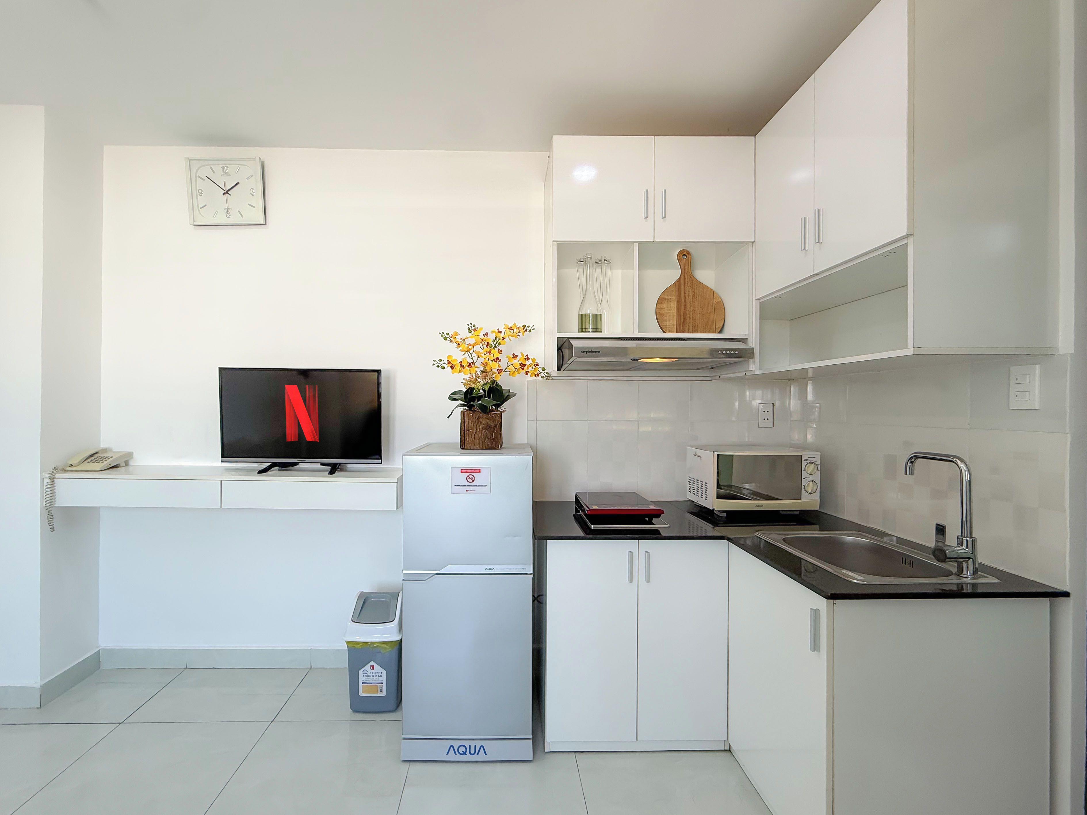 Una cocina moderna con armarios blancos, microondas integrado, un lavabo y un televisor que muestra el logotipo de Netflix.