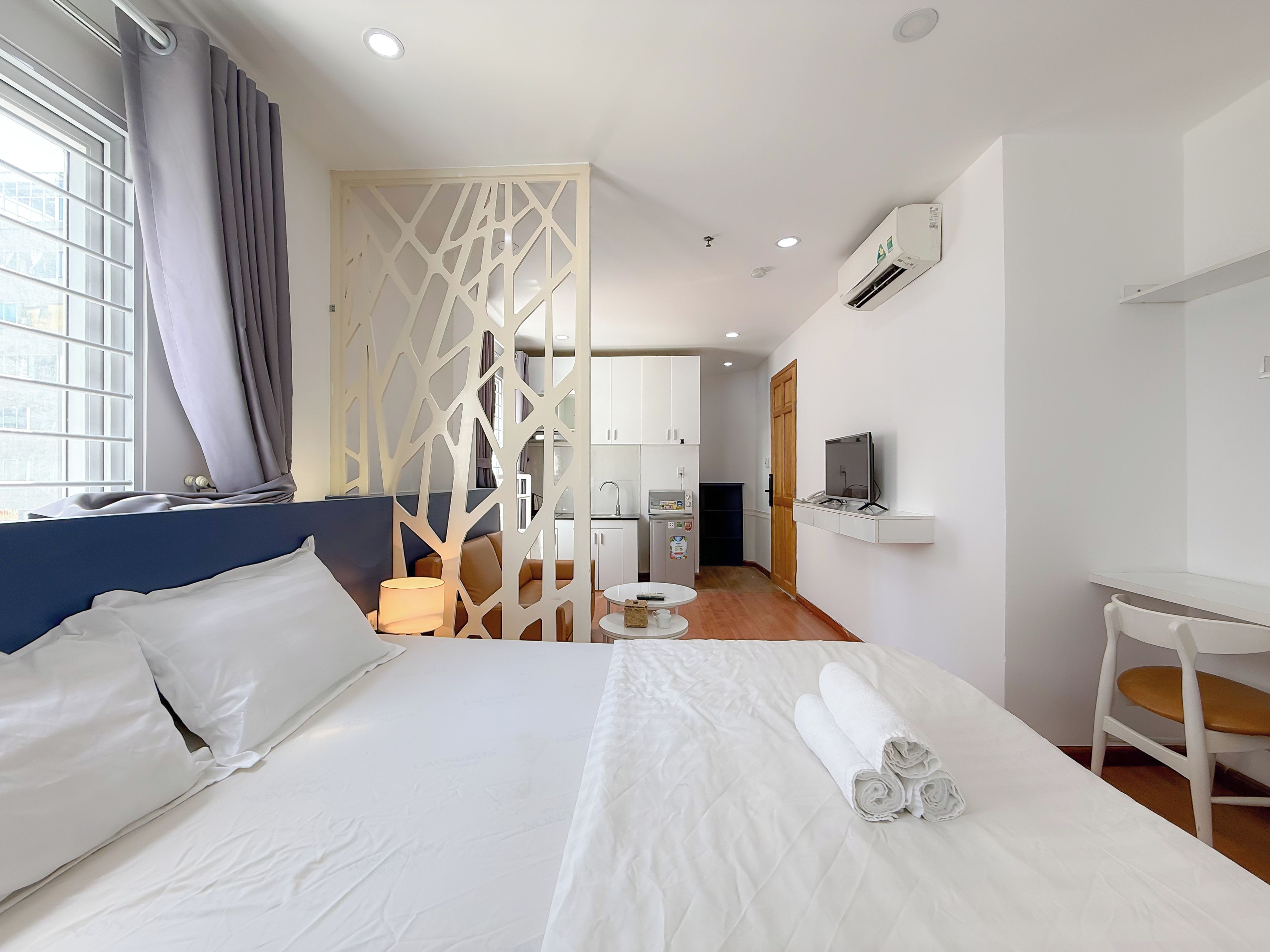 Una habitación de hotel con cama, escritorio, televisor y kitchenette.