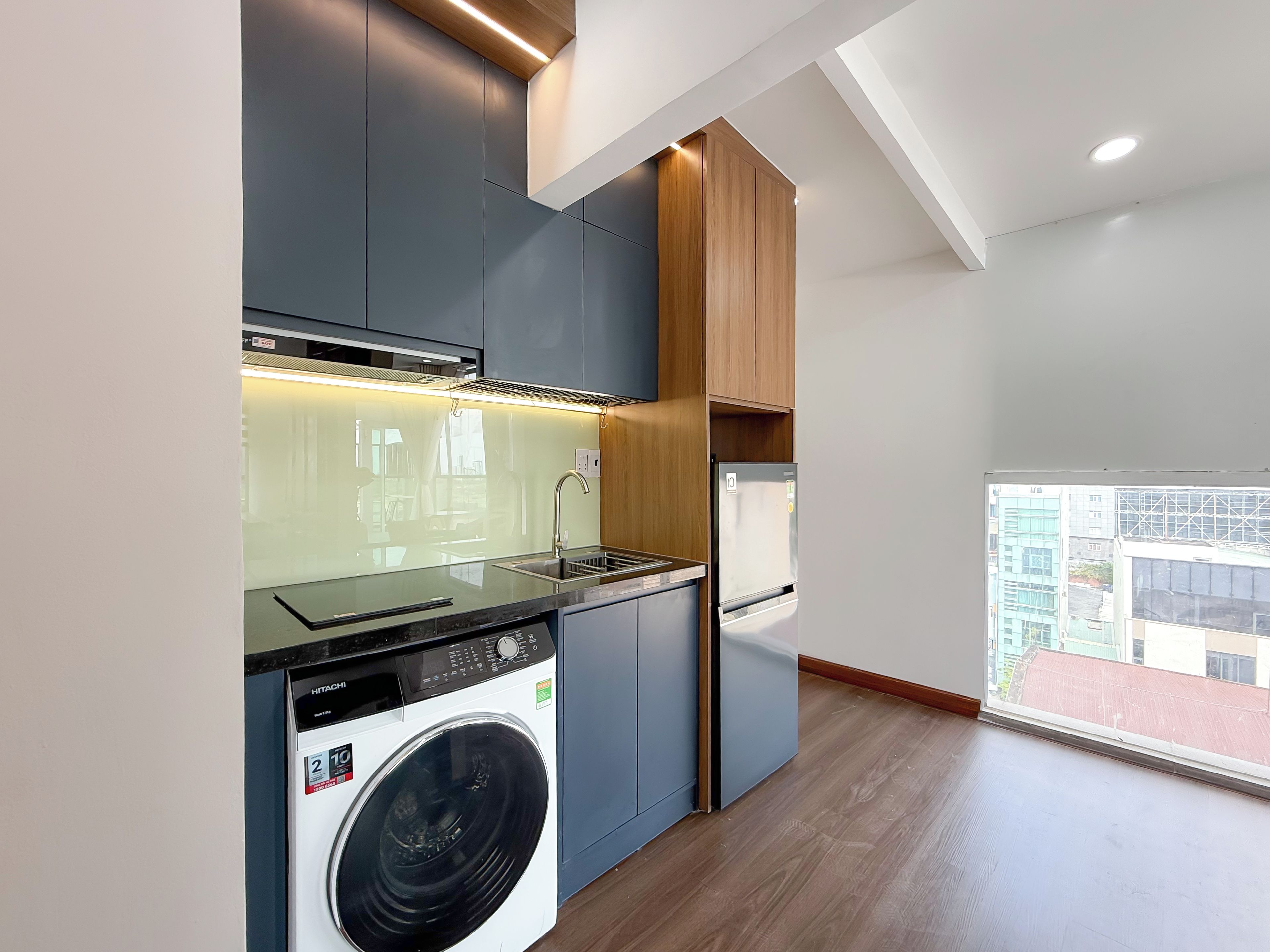 A modern kitchen with a built-in washer, a stainless steel refrigerator, and a window overlooking a cityscape.