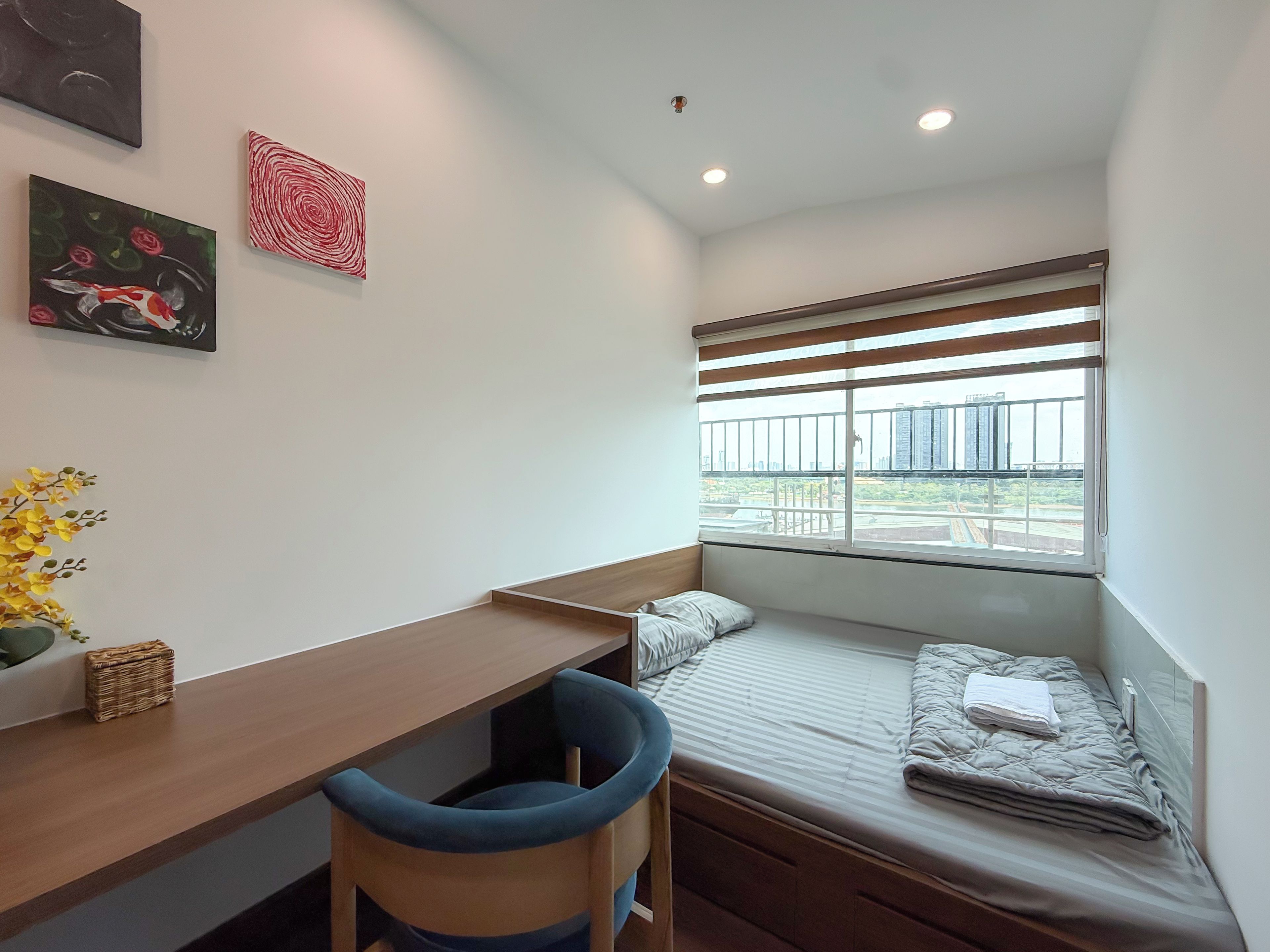 A small room with a bed, a desk, and a window with blinds.