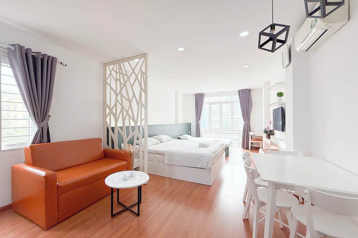 A modern hotel room with a bed, a sofa, a small table, and a desk with chairs.