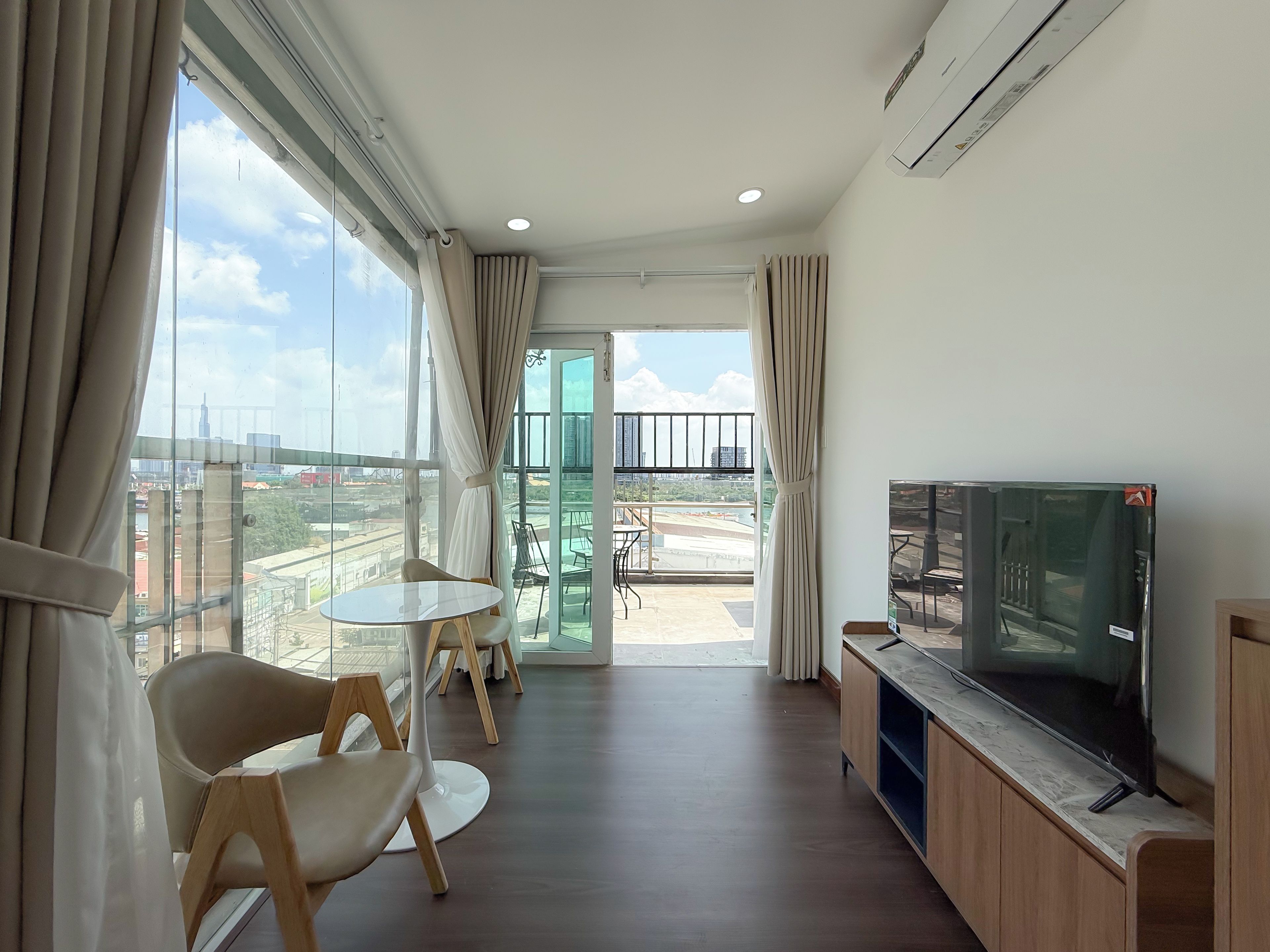 Una sala de estar moderna con un televisor de pantalla plana, una mesa de comedor con sillas y un balcón con vistas a la ciudad.