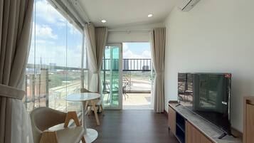 Una sala de estar moderna con un televisor de pantalla plana, una mesa de comedor con sillas y un balcón con vistas a la ciudad.