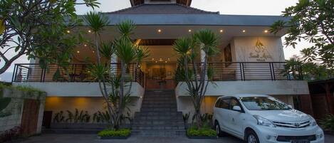 A modern villa with a central staircase, a car parked in front, and a well-maintained garden.
