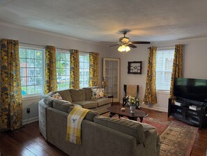 A living room with a sectional sofa, a ceiling fan, a television, and a window with curtains. - Historic 3-bedroom house in downtown Brooklyn Arts district (Wilmington)
