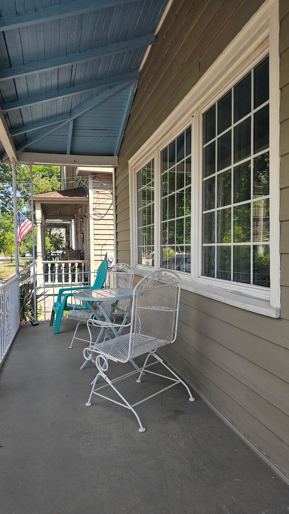 A covered porch with a table and chairs, a view of the street, and a flag.