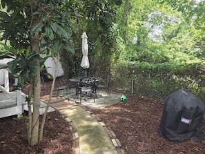 Eine Terrasse im Freien mit Tisch und Stühlen, umgeben von Bäumen und einem weißen Zaun.