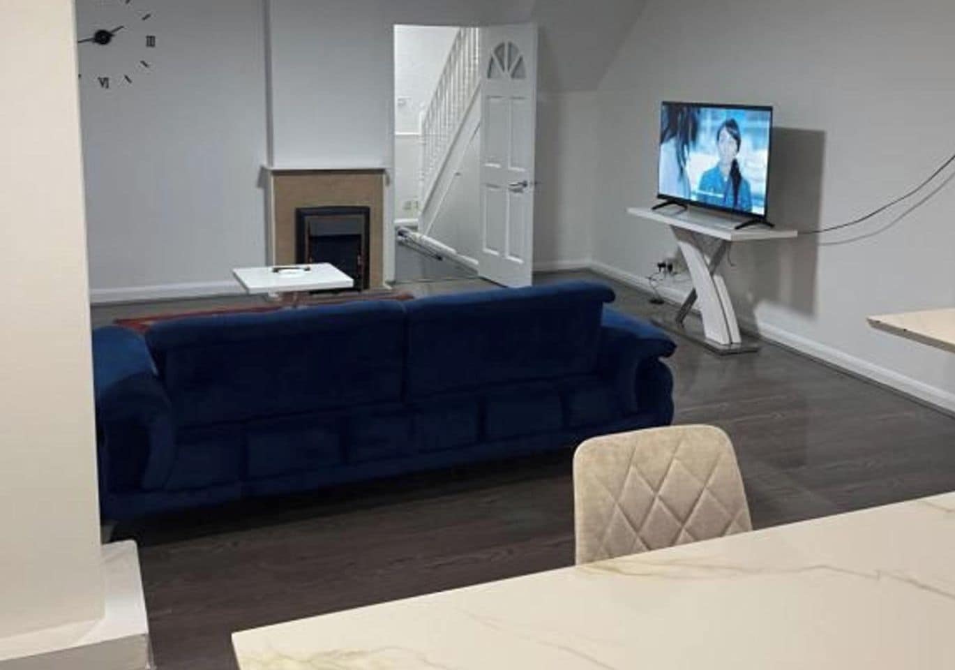 Ein Wohnzimmer mit einem blauen Sofa, einem Fernseher auf einem Schrank, einem Kamin und einer Treppe.