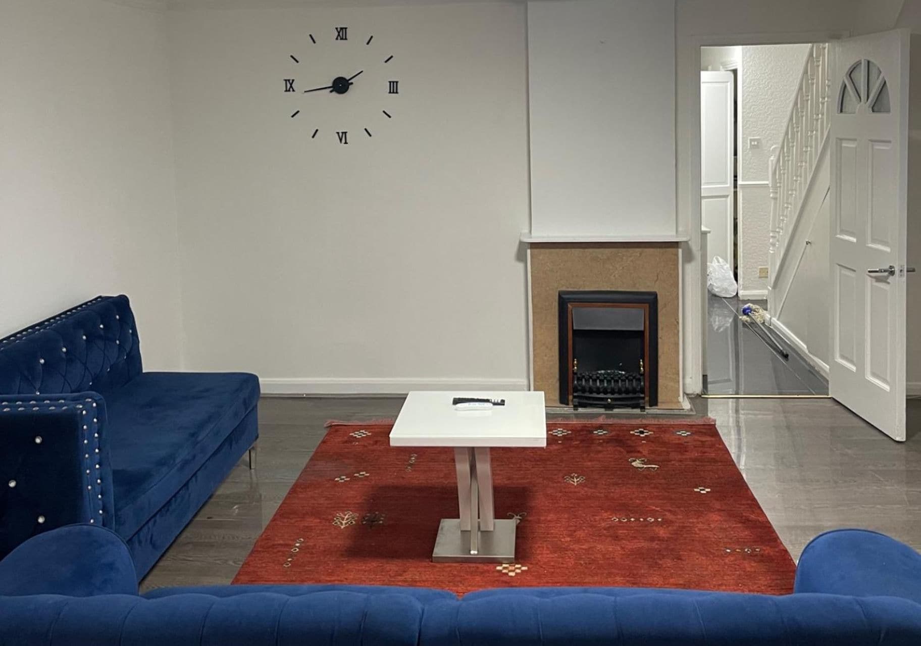 Ein Wohnzimmer mit einem blauen Sofa, einem weißen Tisch, einem roten Teppich und einem Kamin.