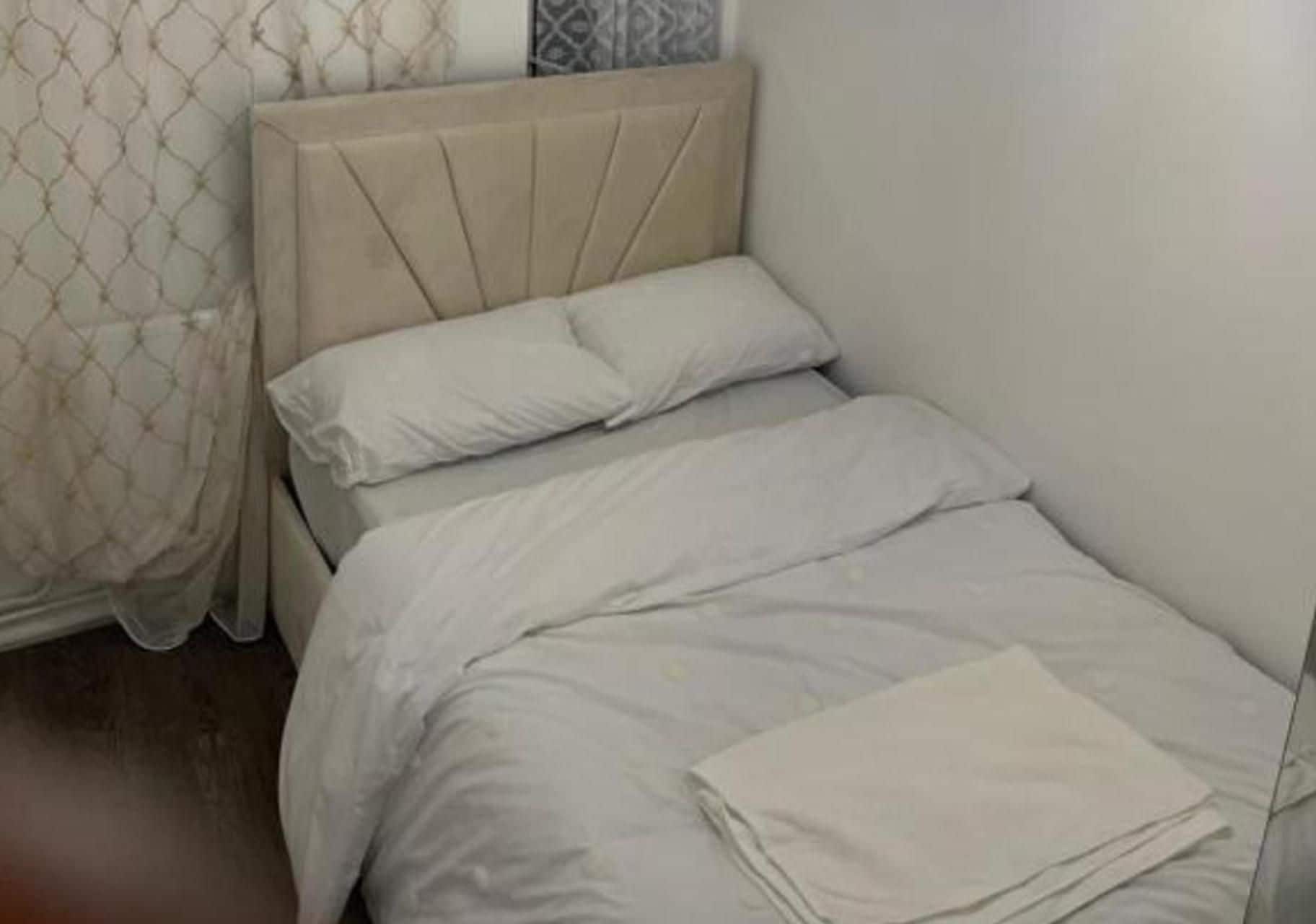 A single bed with a headboard, white bedding, and a folded blanket on the bed.