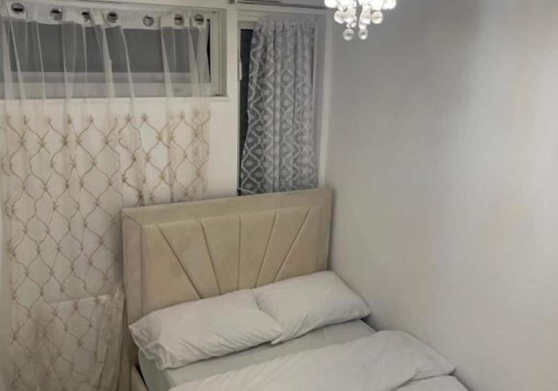 Ein Schlafzimmer mit einem Bett, einem Fenster mit Vorhängen und einer Kristallleuchtre.