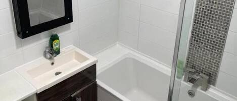 Une salle de bain avec un lavabo blanc, des meubles en bois foncé, un miroir et un espace douche doté d’une porte en verre.