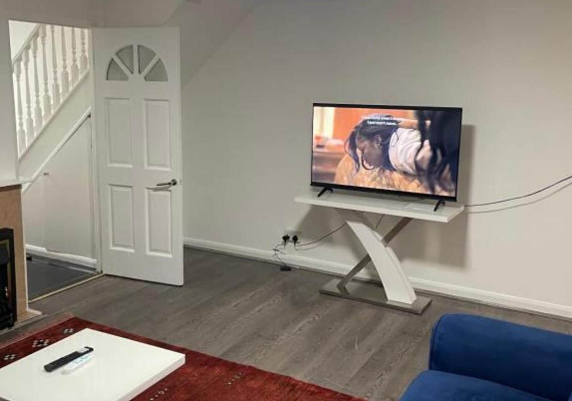 Una sala de estar con un televisor sobre un mueble bajo, una puerta y una escalera.