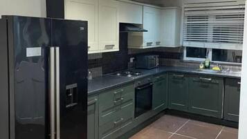 Una cocina con un refrigerador negro, una estufa y un ventanal con persianas.