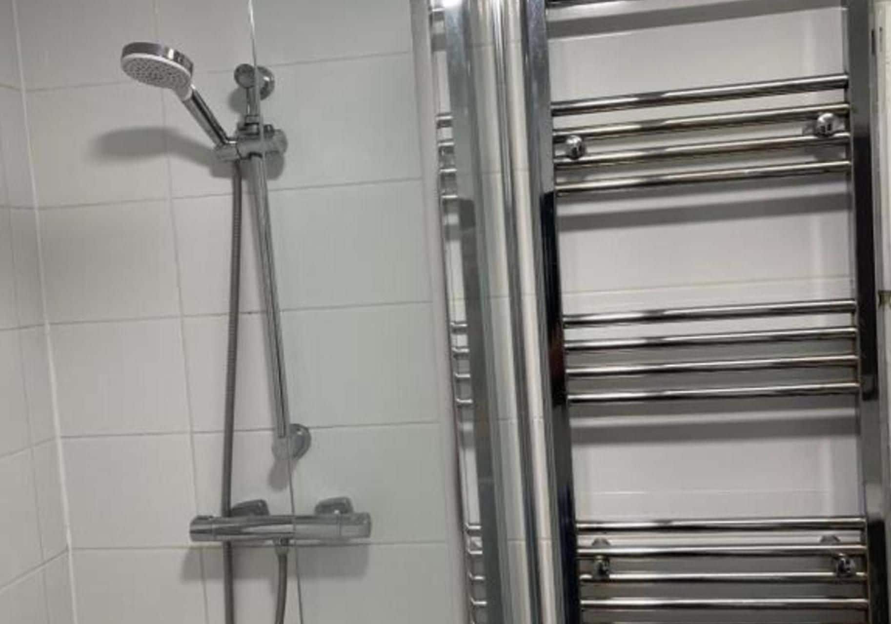 Une douche équipée d’un pommeau de douche à main et d’un robinet mural, ainsi qu’un porte-serviettes en chrome.