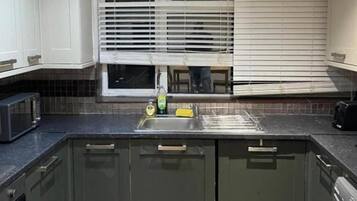 Una cocina con microondas integrado, un fregadero y una ventana con persianas.