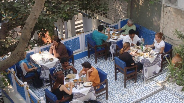 An outdoor dining area with multiple tables and chairs, surrounded by a tiled floor and blue and white patterned walls. - Ray Of Maya Retreat and Resorts (Agra)
