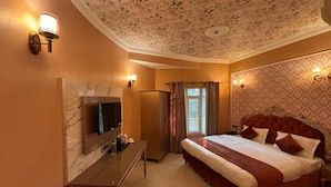 A hotel room with a large bed, a flat-screen TV, a desk, and a window with curtains. - Ray Of Maya Retreat and Resorts (Agra)