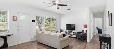Ein geräumiges Wohnzimmer mit einem weißen Sofa, einem Fernseher und einem Deckenventilator.
