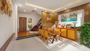 A modern reception area with a wooden reception desk, a dining table with chairs, a staircase, and a large painting on the wall. - Omega Hotel (Da Nang Municipality)