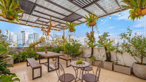 An outdoor terrace with a city view, featuring a table and chairs, potted plants, and hanging plants. - Omega Hotel (Da Nang Municipality)