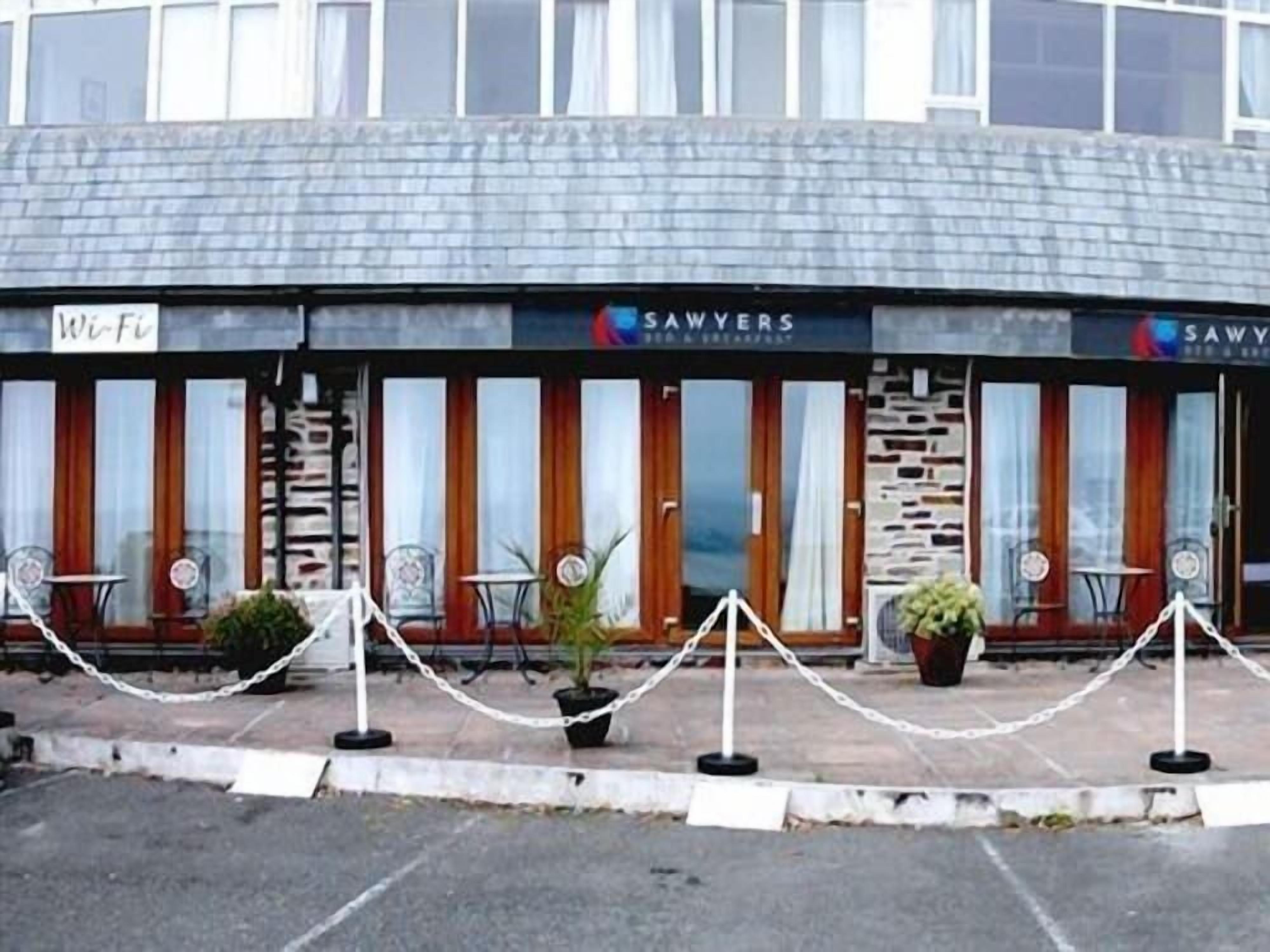 Un edificio con un letrero que dice 'SAWVERS', indicando un restaurante o cafetería. Hay áreas de estar al aire libre con mesas y sillas.