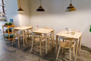 A dining area with wooden tables and chairs, pendant lighting, and a plant on a shelf. - Homey House (Taipei)