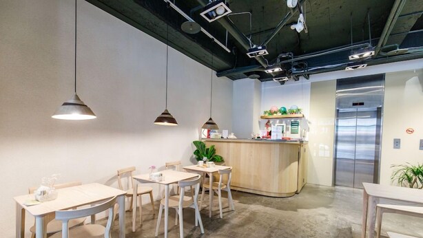 A modern office space with a central counter, multiple tables and chairs, and a visible elevator. - Homey House (Taipei)