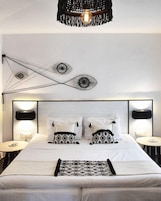 Un dormitorio moderno con cama blanca, almohadas estampadas, una manta blanco y negro, e instalación artística única en la pared.