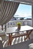 Un balcón con mesa y sillas, una planta en maceta y vistas al mar y edificios.