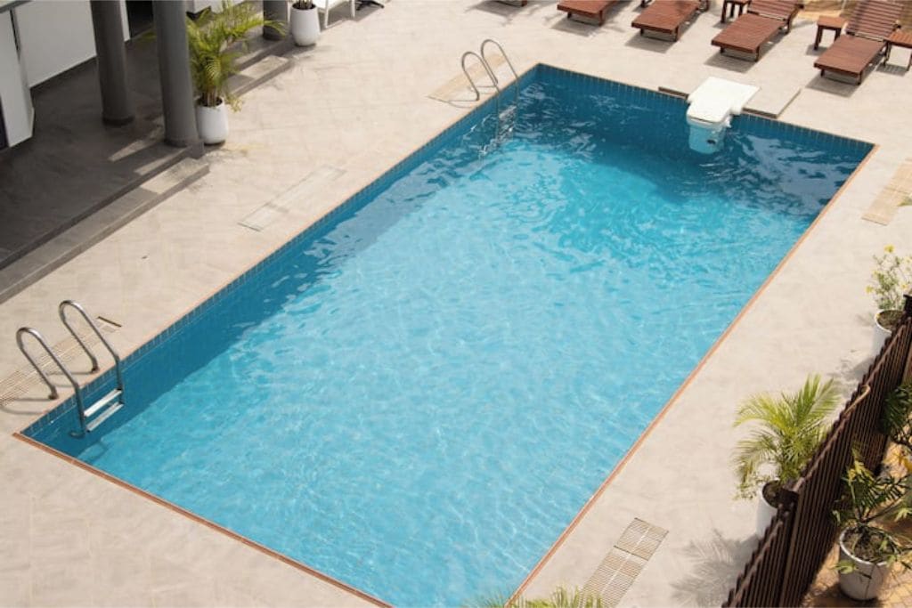 A rectangular swimming pool with a clear blue water surface, surrounded by lounge chairs and potted plants.