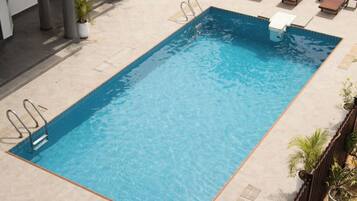 A rectangular swimming pool with a clear blue water surface, surrounded by lounge chairs and potted plants.