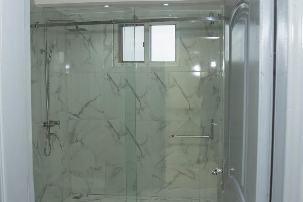 A glass-enclosed shower with a marble wall, a small window, and a towel rack.