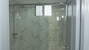 Een douche met glazen wanden, een marmeren muur, een klein raam en een handdoekhouder.