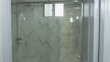 A glass-enclosed shower with a marble wall, a small window, and a towel rack.
