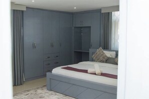 A bedroom with a bed, built-in wardrobe, and a window with curtains. - The Africa Reach (Accra)