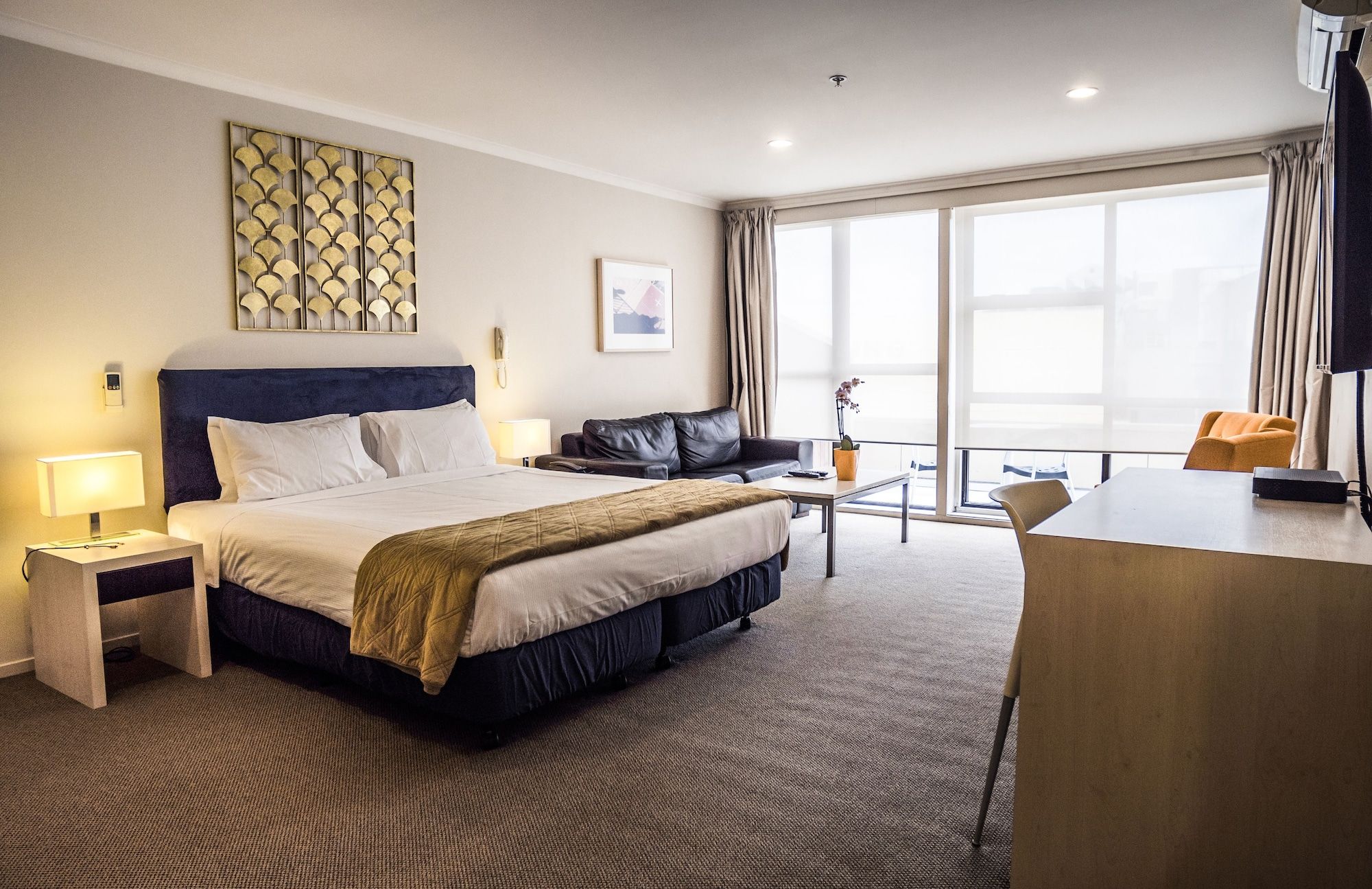 A hotel room with a bed, a desk, a sofa, and a large window.