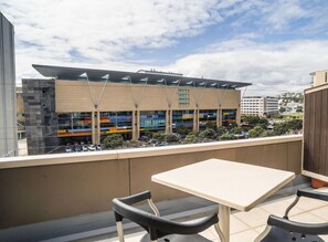 Un balcón con una mesa y sillas, con vista a un edificio moderno de varios pisos y un área de estacionamiento.