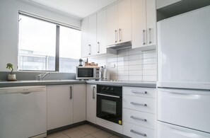 Una cocina moderna con armarios blancos, horno empotrado, microondas y refrigerador.