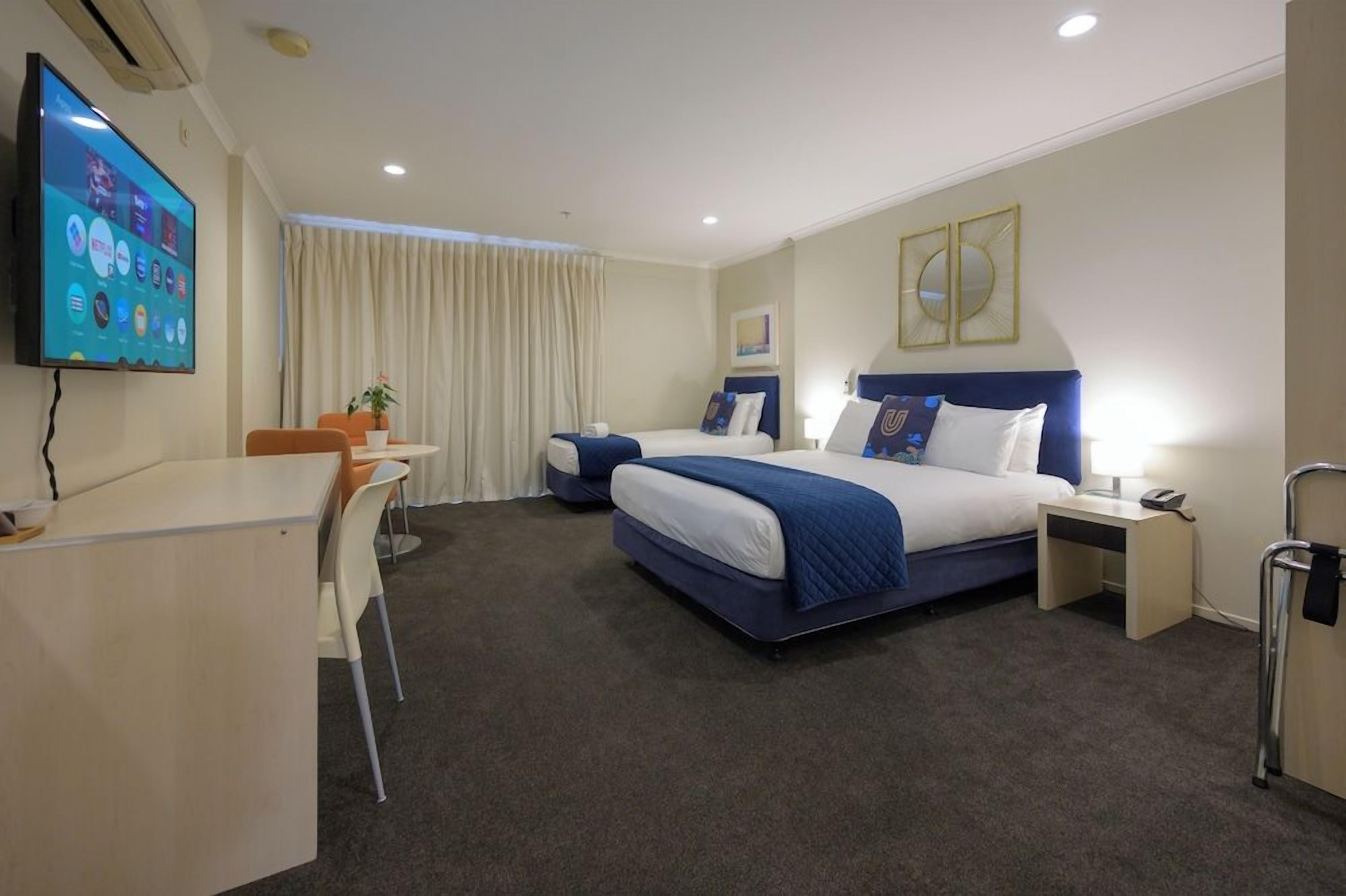 A hotel room with a bed, desk, chair, and a television mounted on the wall.