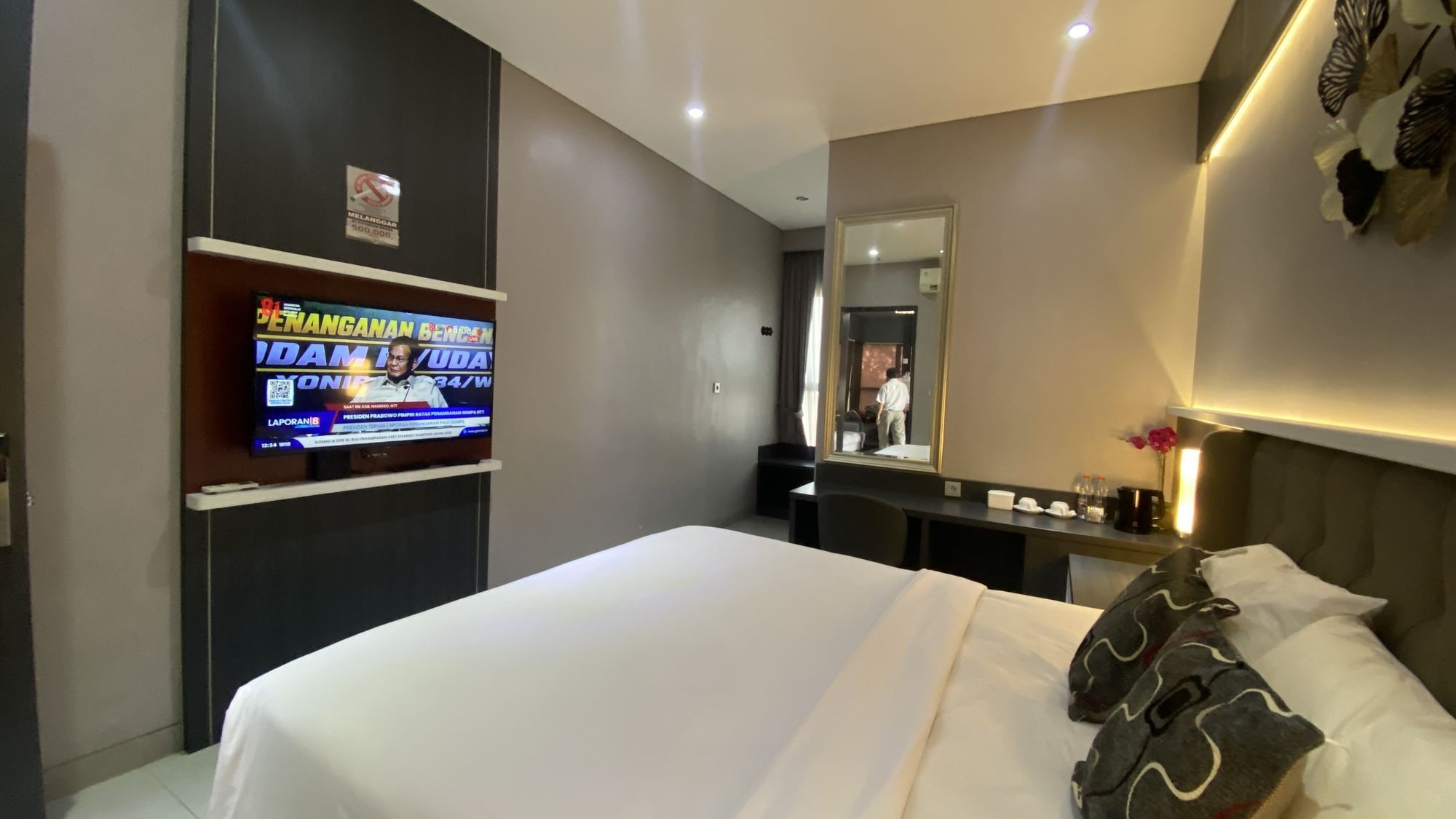 Habitación de hotel con cama, escritorio, televisor y espejo.