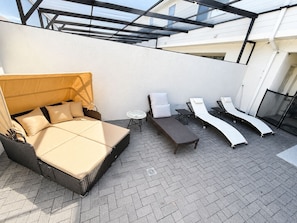 A rooftop patio with a bed, lounge chairs, and a small table.