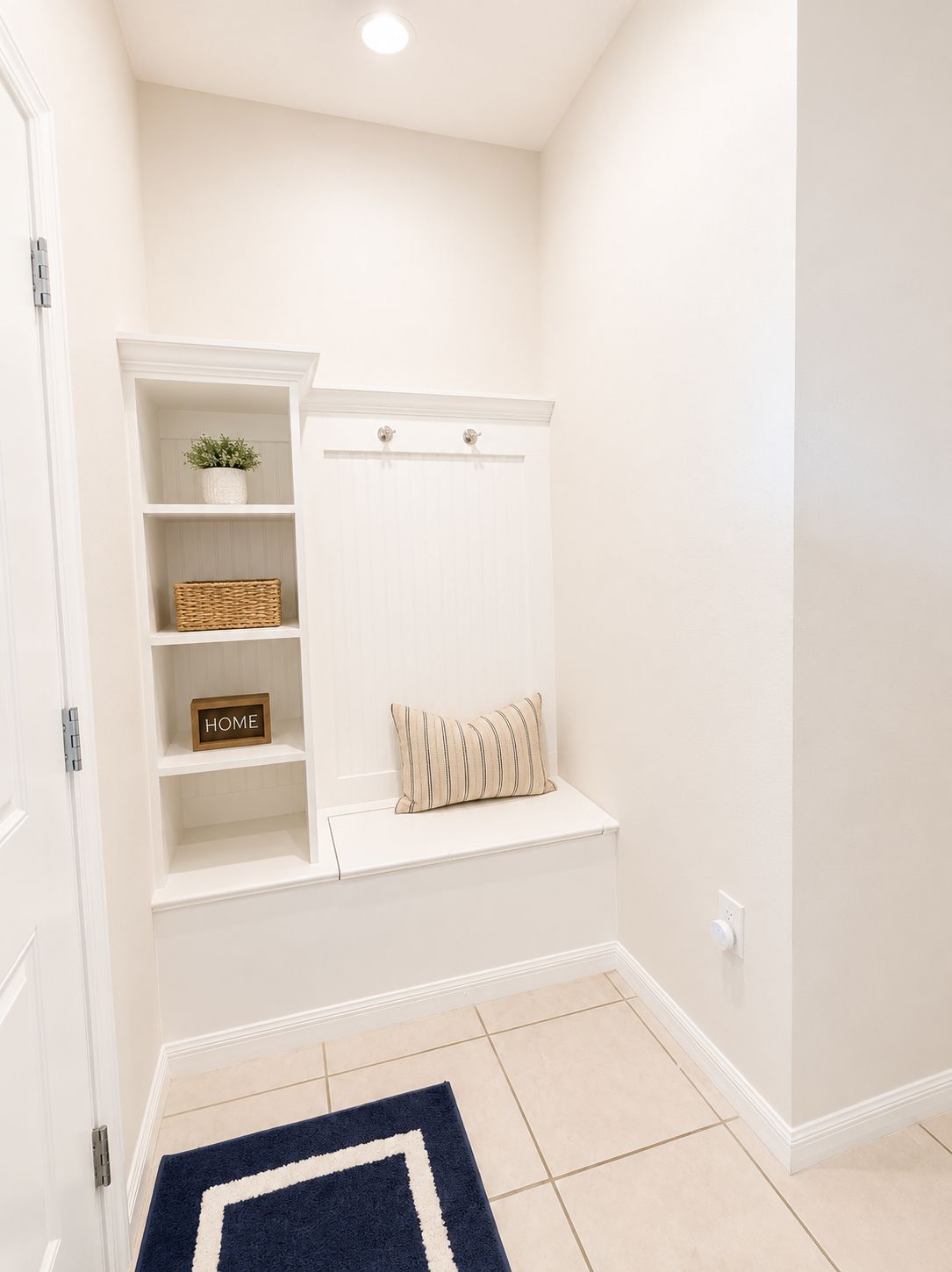 A hallway with a white bench, shelves with a plant, a wicker basket, and a 'HOME' sign.