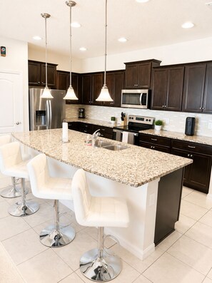 A modern kitchen with dark wood cabinets, stainless steel appliances, a granite countertop, and pendant lighting.